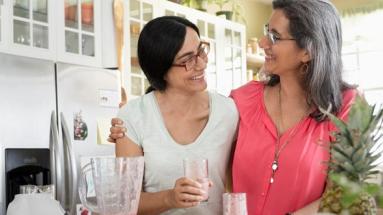 Dos mujeres en una cocina se miran con un zumo de piña en la mano
