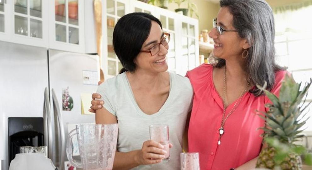 Dos mujeres en una cocina se miran con un zumo de piña en la mano